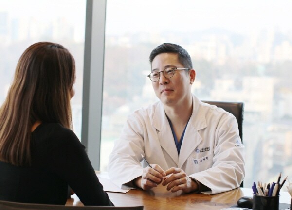 Dr. Rhee Sewhan of Grand Plastic Surgery in a rhinoplasty consultation, with the Seoul skyline behind the window